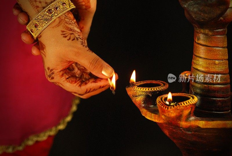 印度排灯节(Diwali Deepawali)的横向照片，一位女士，带着指甲花或曼海蒂(mehndi)和一个巨大的金色康康灯饰米提或赤陶瓦蒂亚(terracotta diya)，火柴棍在黑色背景上